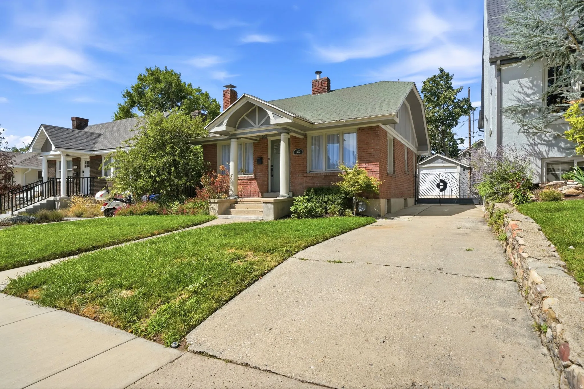 Brick exterior with a green roof, concrete driveway, stone retaining wall, and a detached garage structure