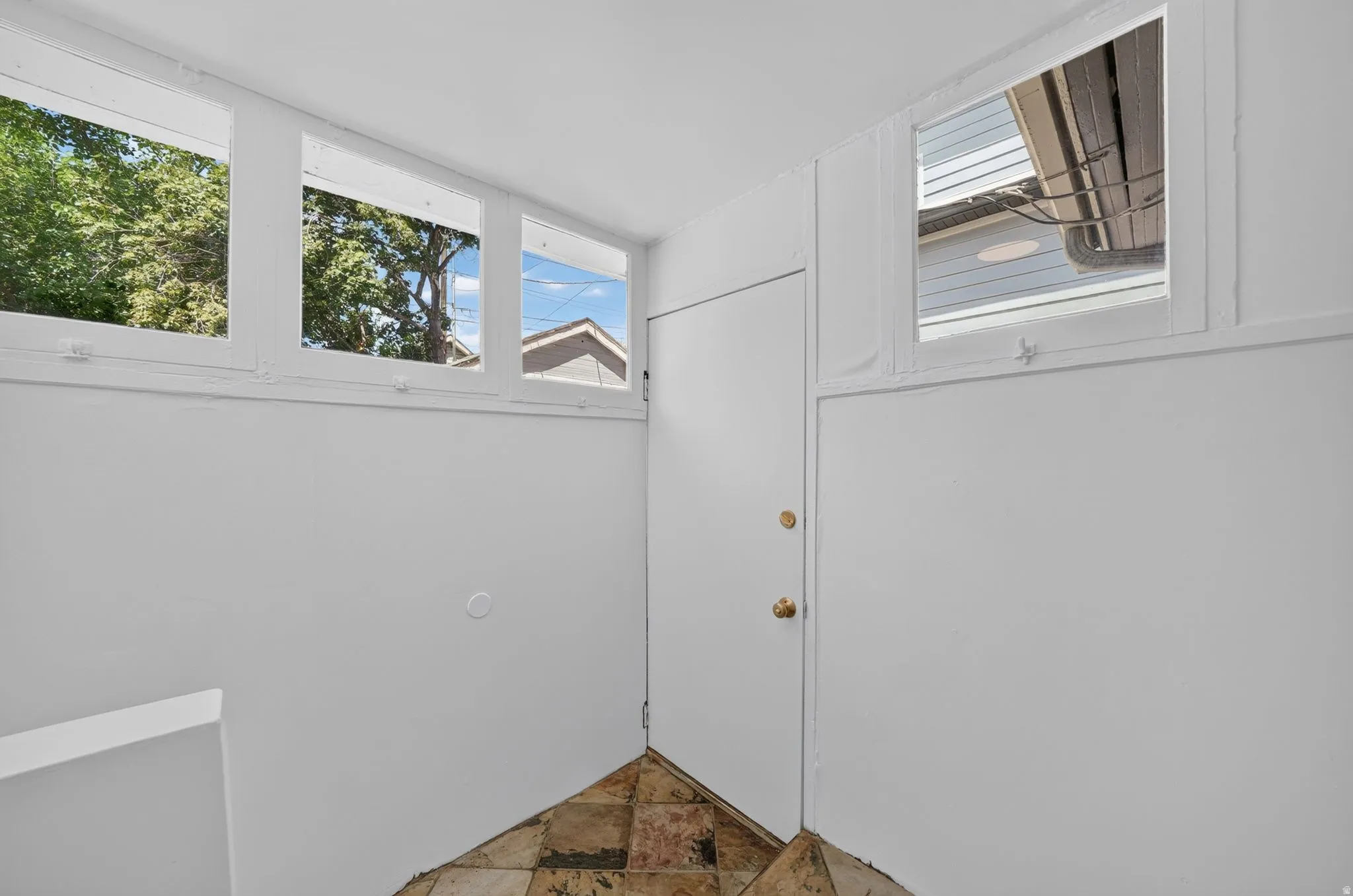 White painted interior with high-set windows, a solid panel door with brass hardware, and a tile floor