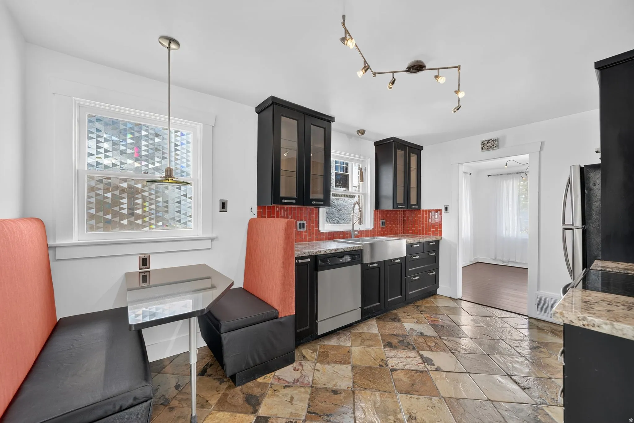 Kitchen featuring slate tile flooring, black cabinetry, a farmhouse sink, and a red tile backsplash