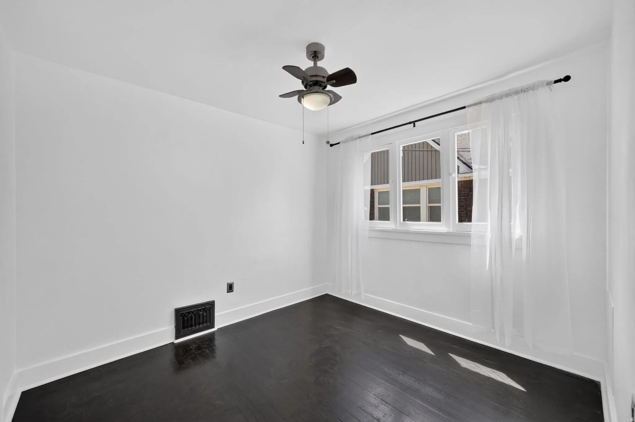 Dark wood-finish flooring, white walls, ceiling fan with integrated lighting, and multiple pane window