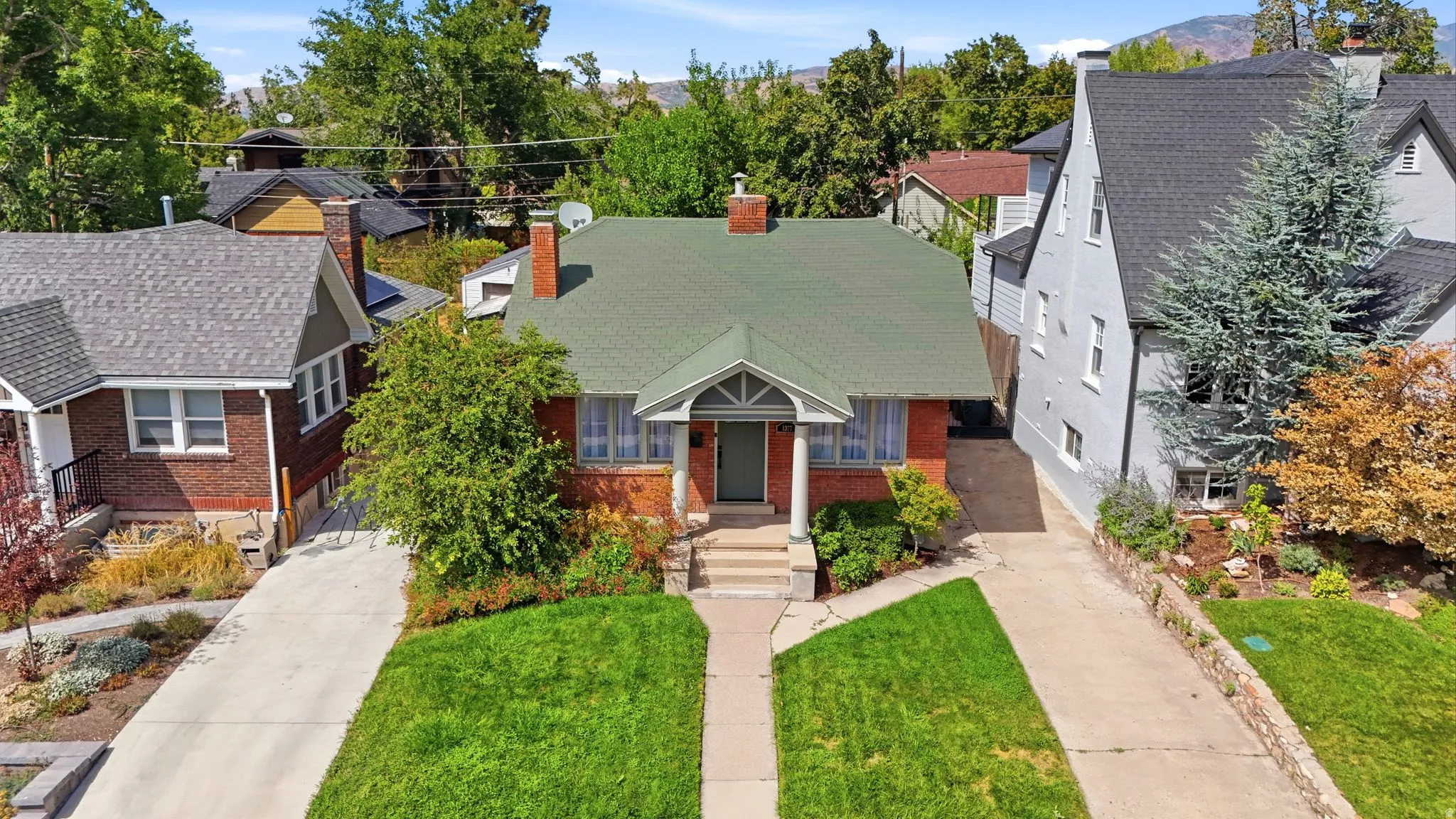Brick exterior with a green shingle roof, established landscaping, and a concrete driveway