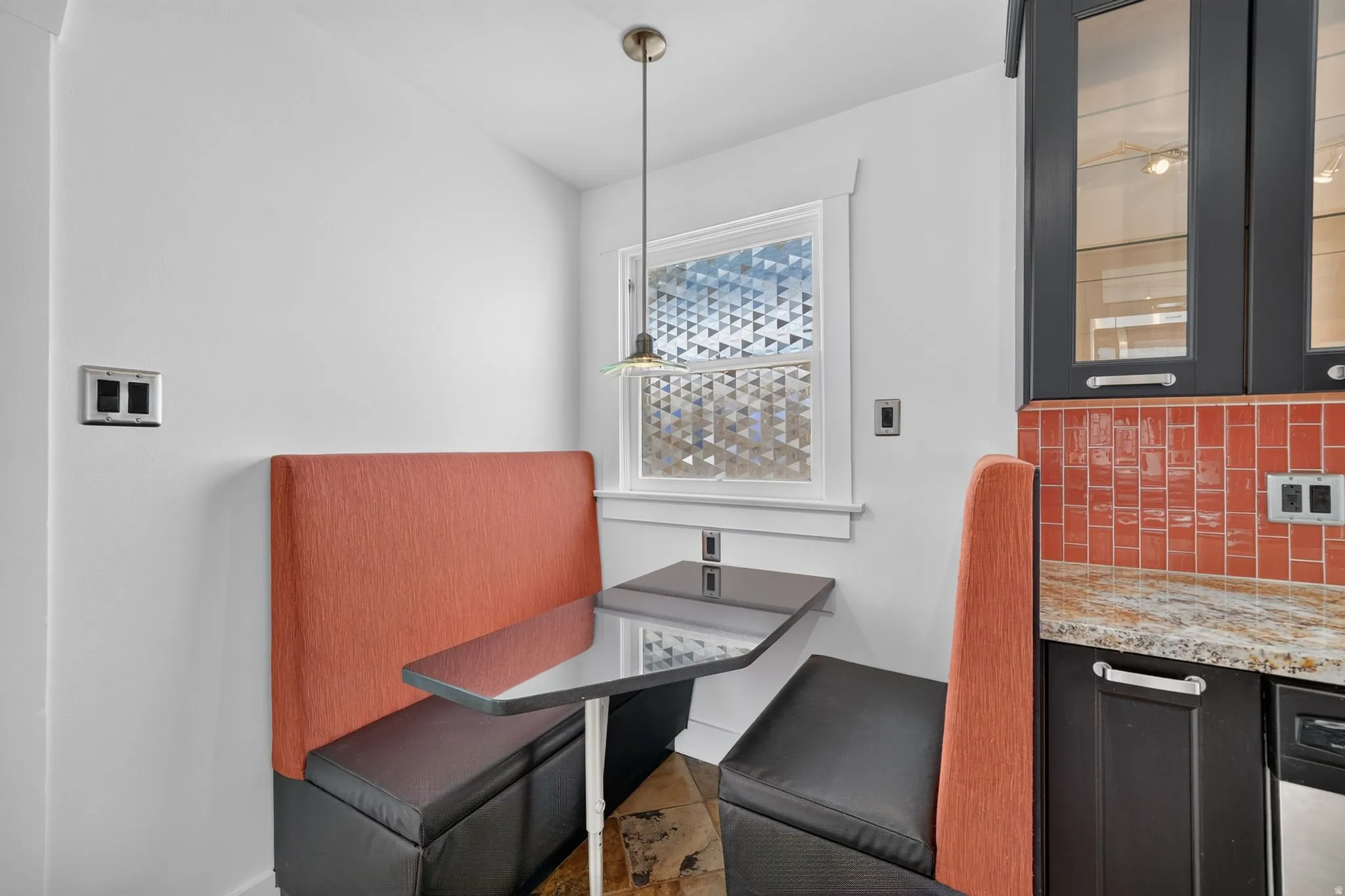 Built-in banquette seating with a black tabletop, pendant lighting, red subway tile backsplash, and granite countertops