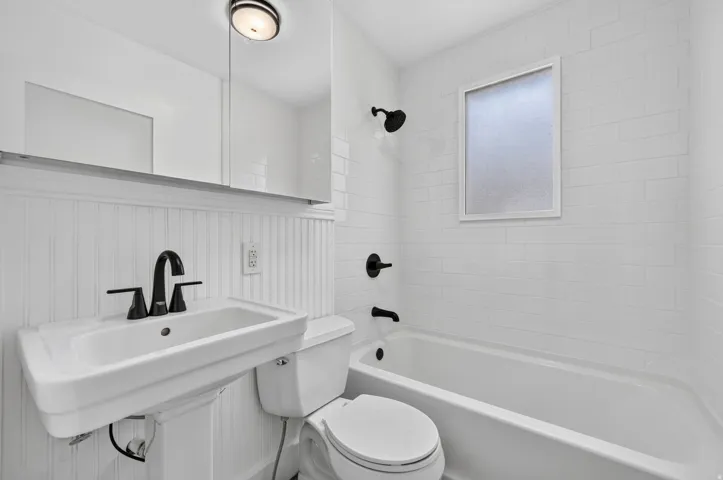 Pedestal sink with matte black faucet, subway tile shower surround, shower/tub combination, and frosted window