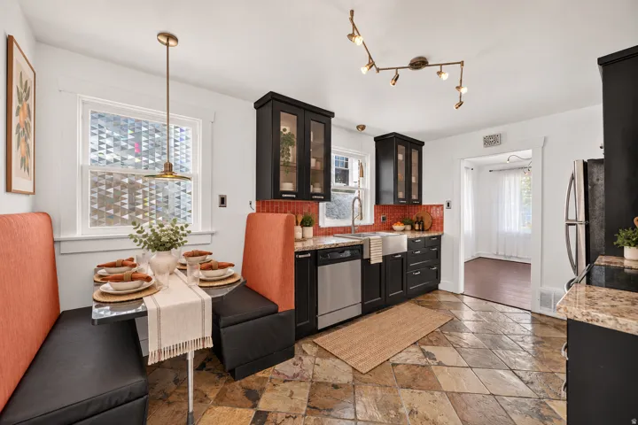 Kitchen featuring natural stone flooring, dark wood-finish cabinetry, a red tile backsplash, and stainless steel appliances