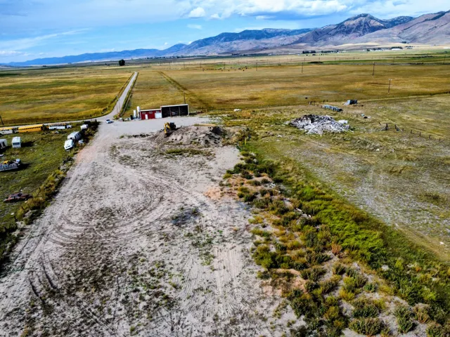 Expansive rural property featuring a long access road, a red and white utility building, and distant mountain backdrops