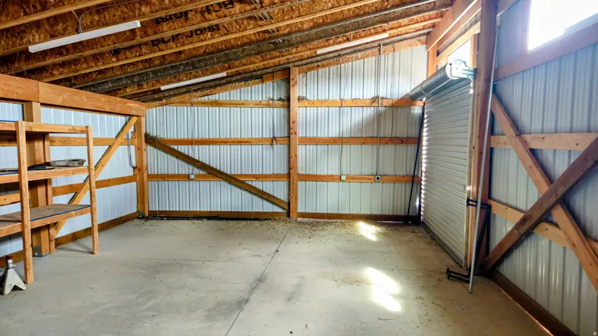 Concrete flooring, exposed wood beam construction, metal corrugated wall panels, built-in wooden shelving, and overhead fluorescent lighting