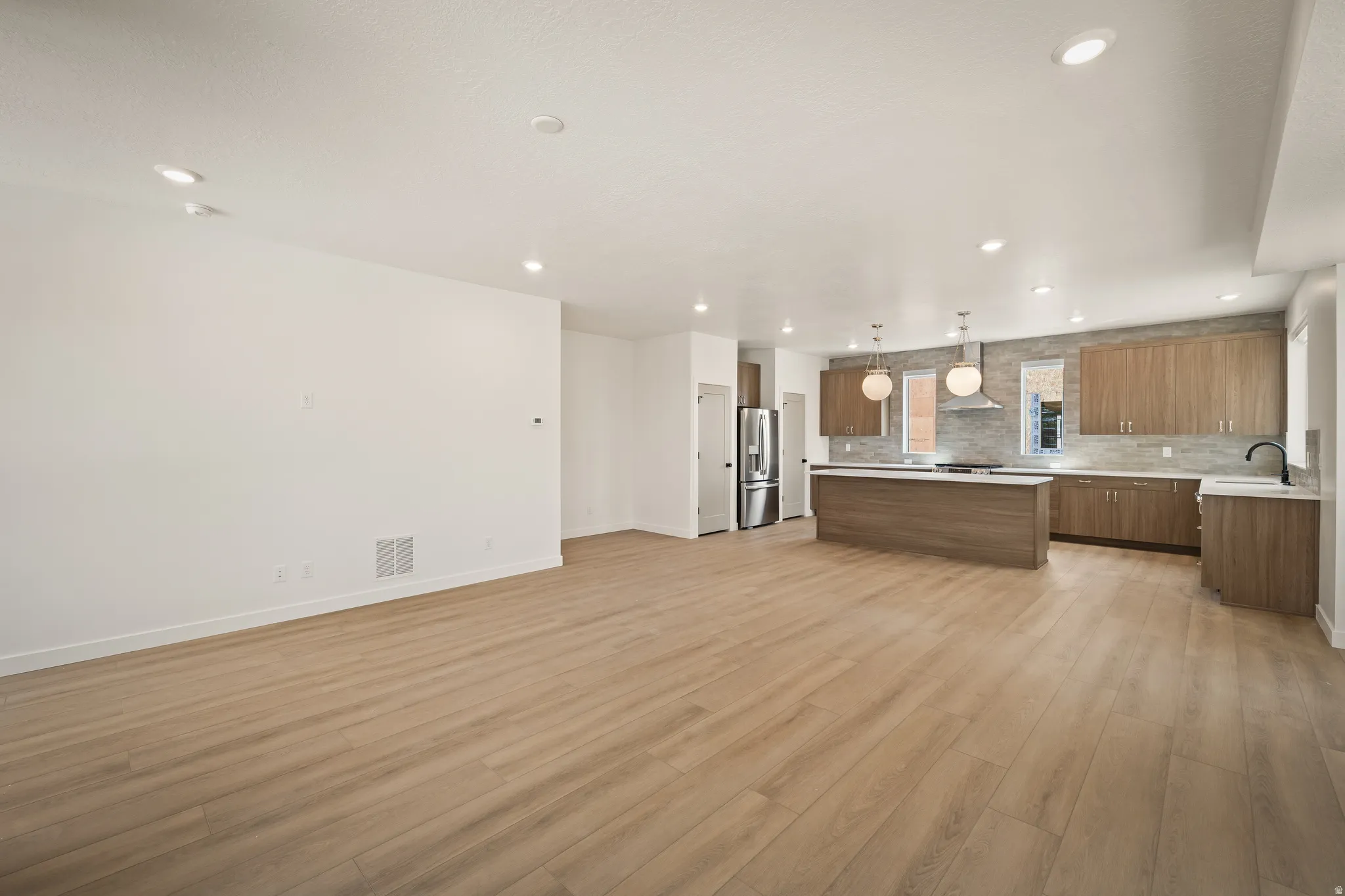 Open-concept living space featuring wood-finish flooring, recessed lighting, and a kitchen with stainless steel appliances, an island, and pendant lighting