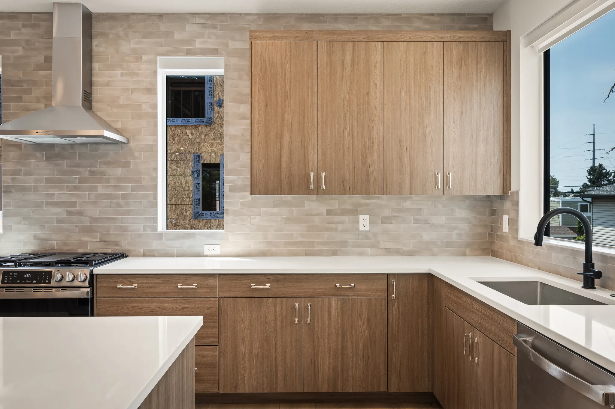 Wood-finish cabinetry, stainless steel appliances, light-toned brick backsplash, white countertops, and a matte black faucet