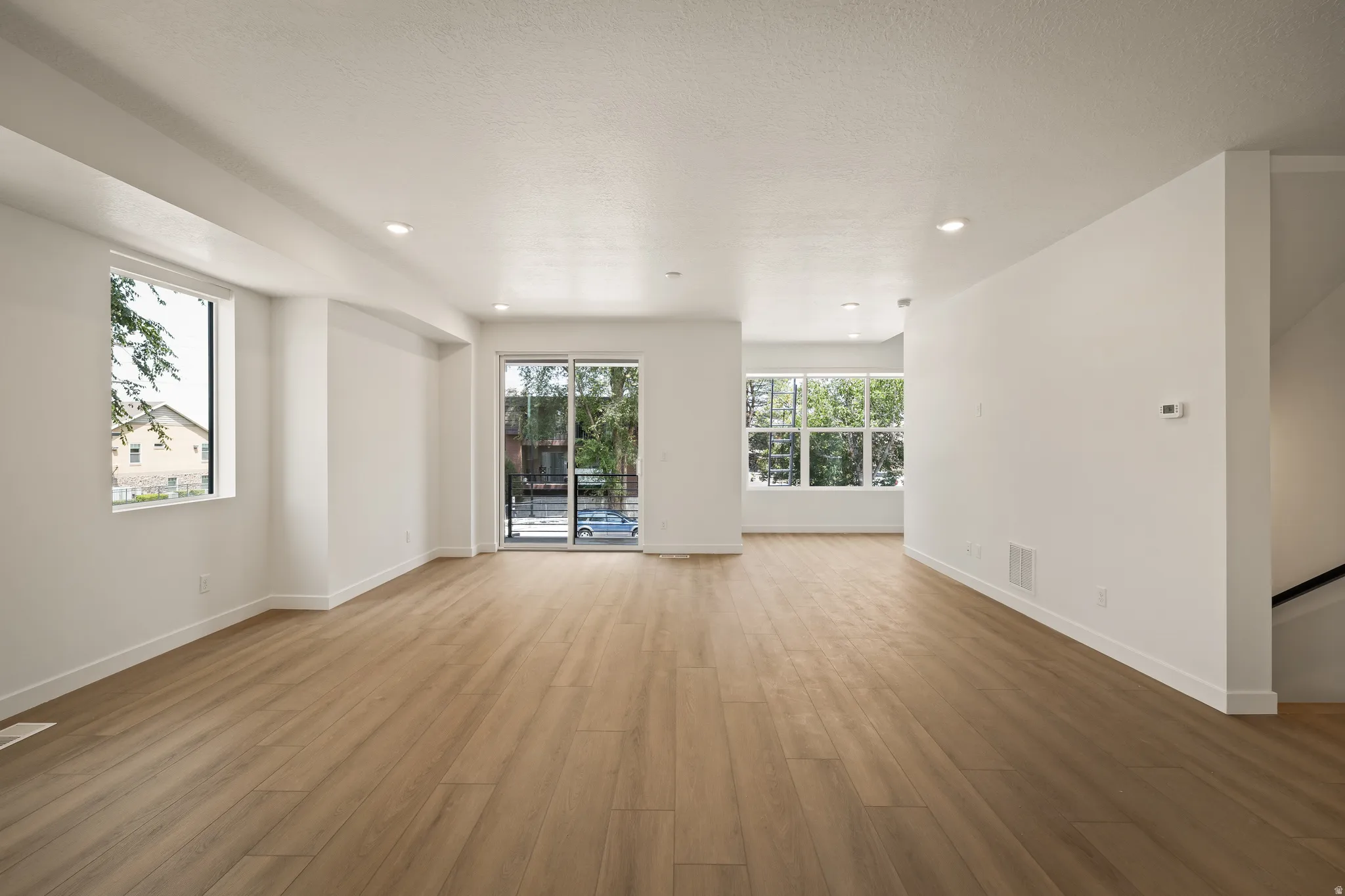 Expansive open-concept living area featuring wood-finish flooring, recessed lighting, large windows, and a sliding glass door