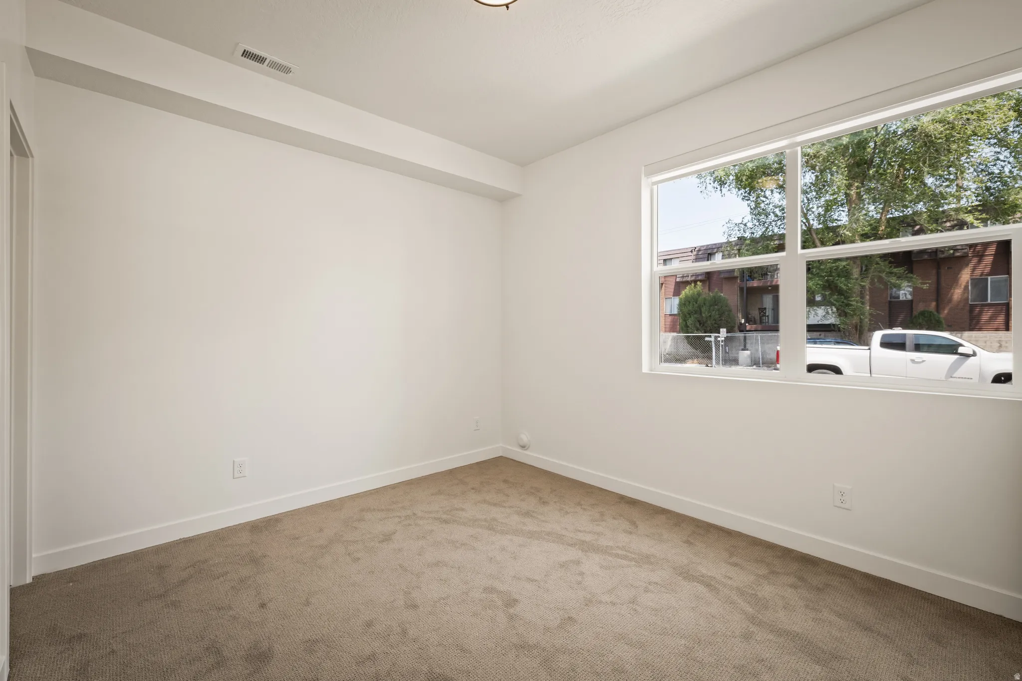 Neutral wall paint, plush carpeting, recessed ceiling light, and a large multi-pane window