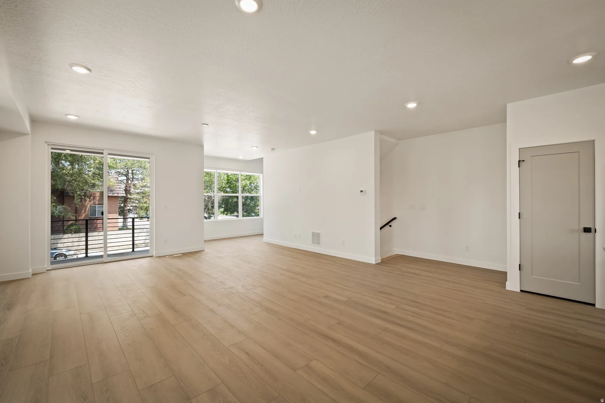 Recessed lighting, wood-finish flooring, sliding glass door, white walls, and a modern interior door
