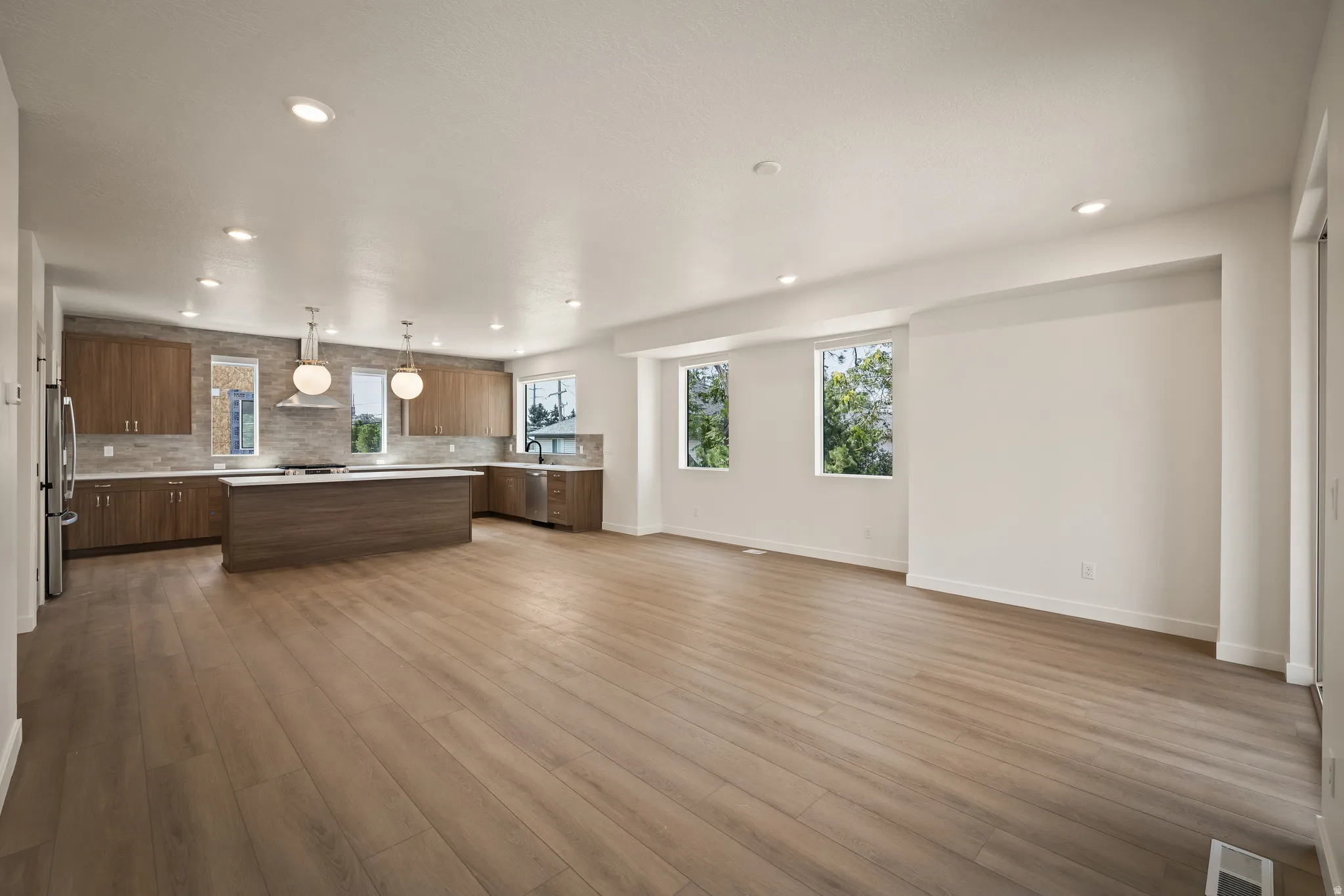 Expansive open-concept living area featuring wood-finish flooring, recessed lighting, and multiple windows