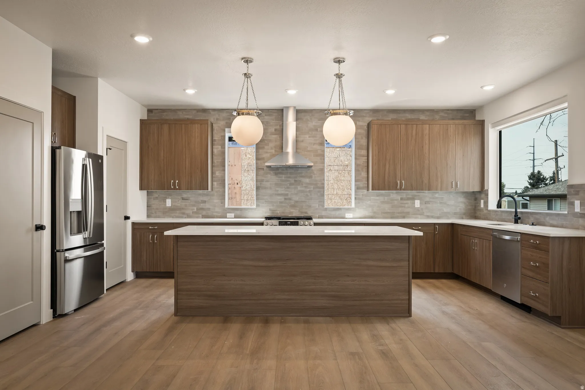 Spacious kitchen featuring wood-finish flooring, a large island with a light-toned countertop, stainless steel appliances, and a tiled backsplash