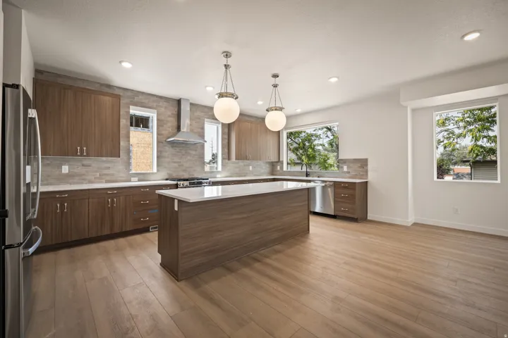 Modern kitchen featuring wood-finish cabinetry, a large center island with a white countertop, stainless steel appliances, and a tile backsplash