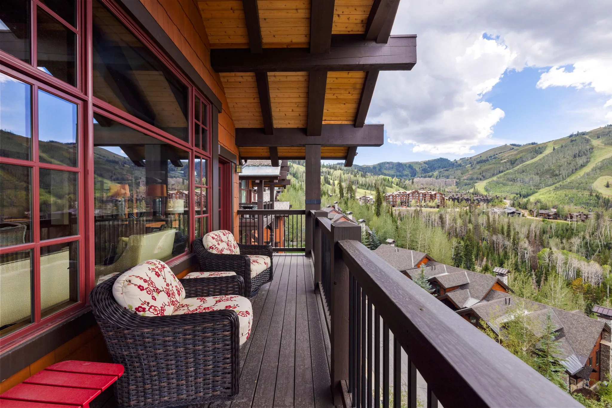 Expansive balcony featuring composite decking, a wood-beam ceiling, and large red-framed windows