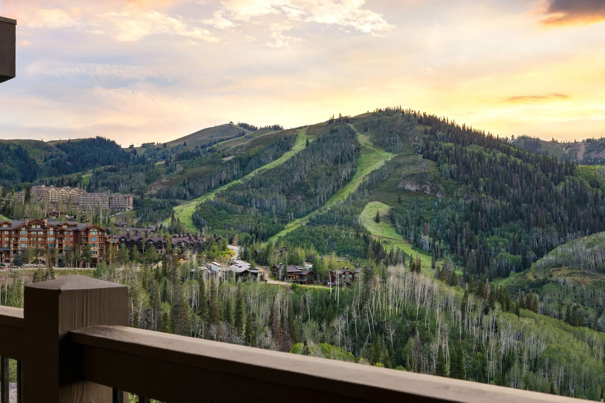 Wood railing with a mountain backdrop, featuring ski slopes, and surrounding residences