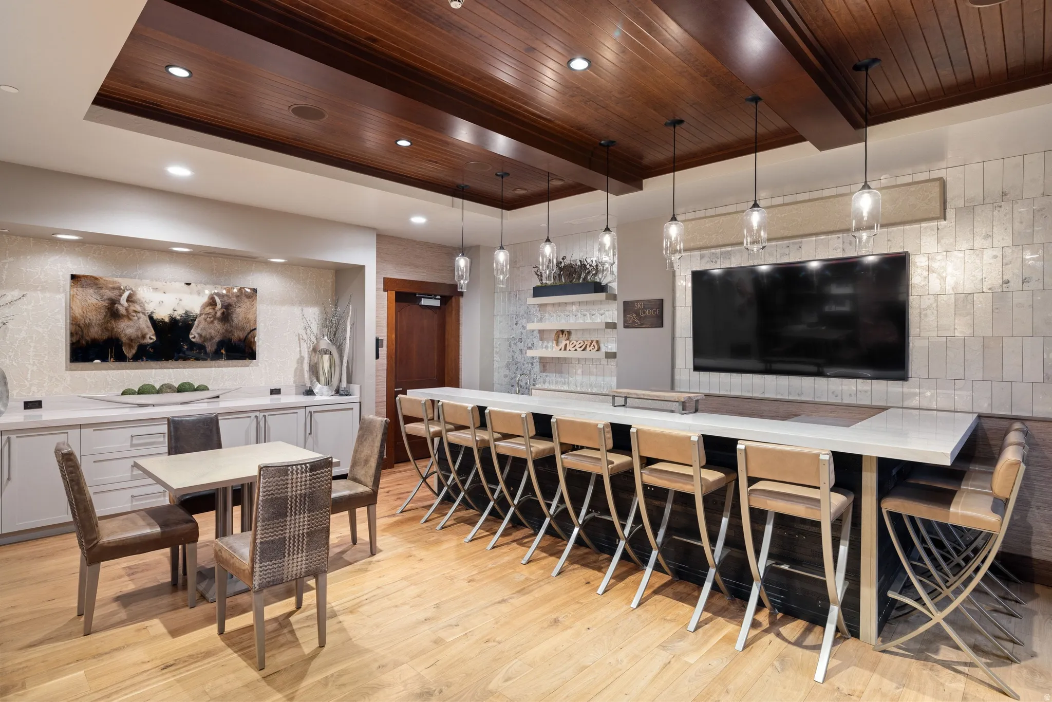 Wood-finish flooring, wood-paneled ceiling with recessed lighting, large custom bar with pendant lighting, built-in cabinetry, and wall-mounted display