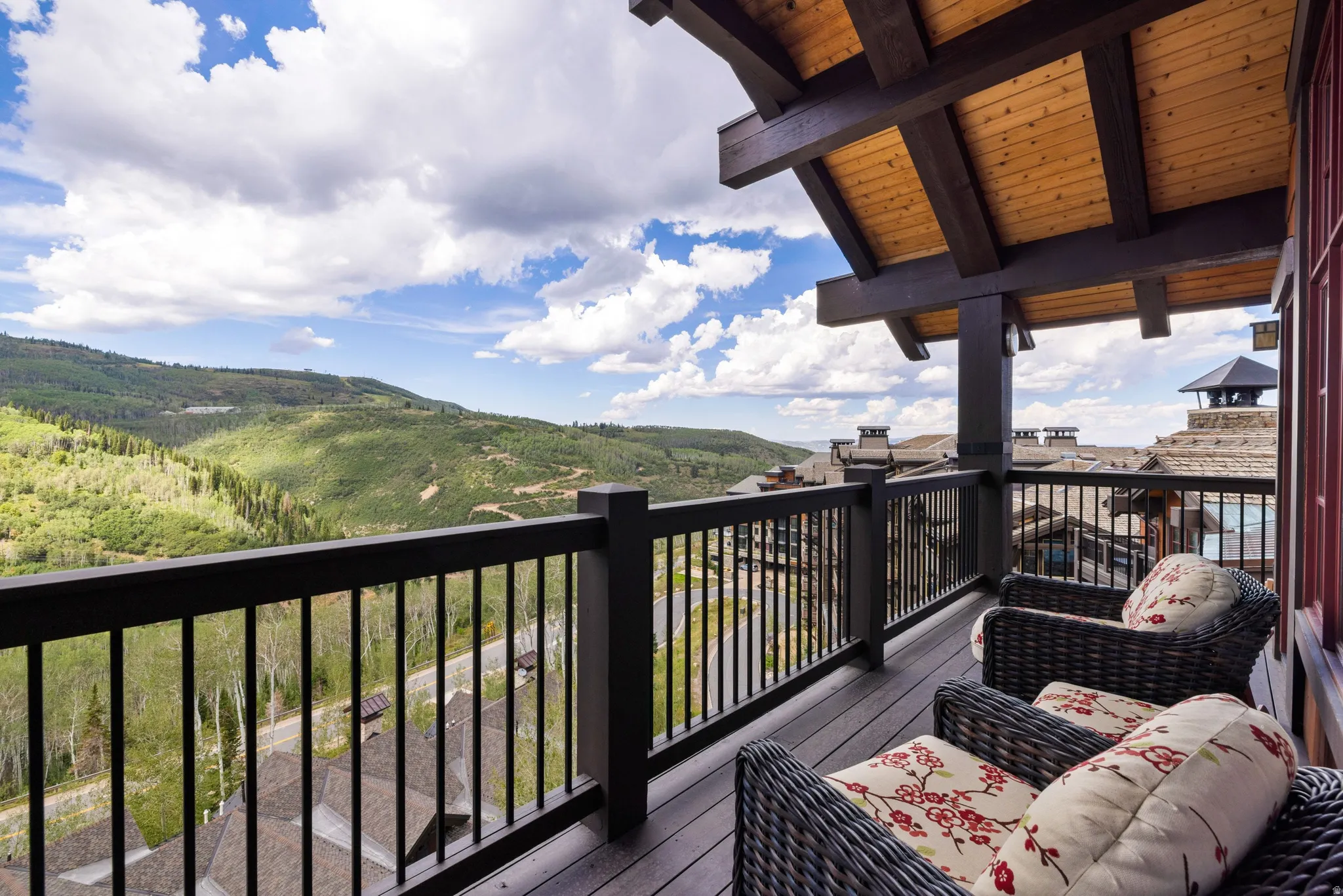 Wood-beamed balcony ceiling, black railing, composite decking, and mountain scenery