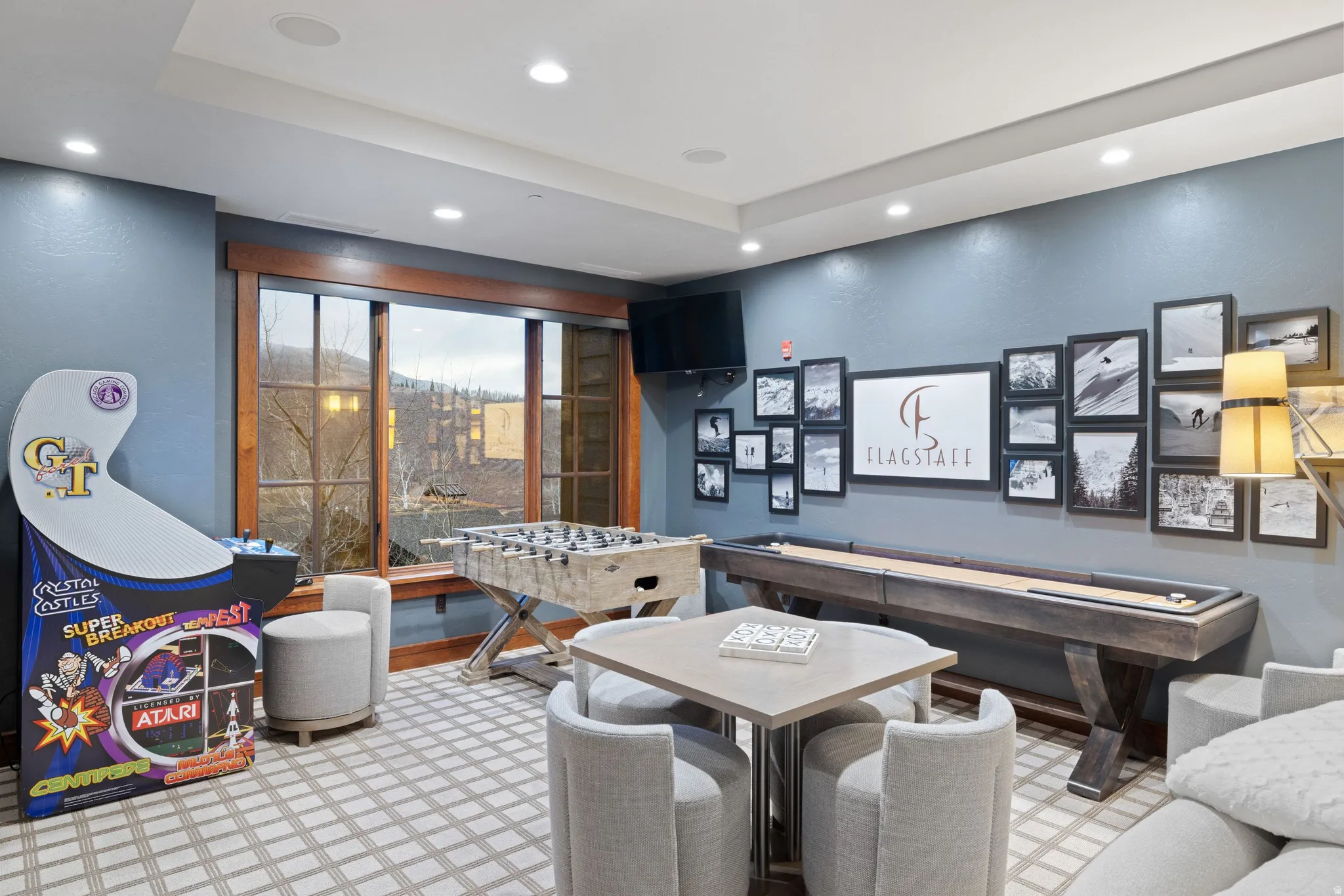 Recessed lighting, large picture windows with dark wood trim, patterned area rug, and a wall-mounted television