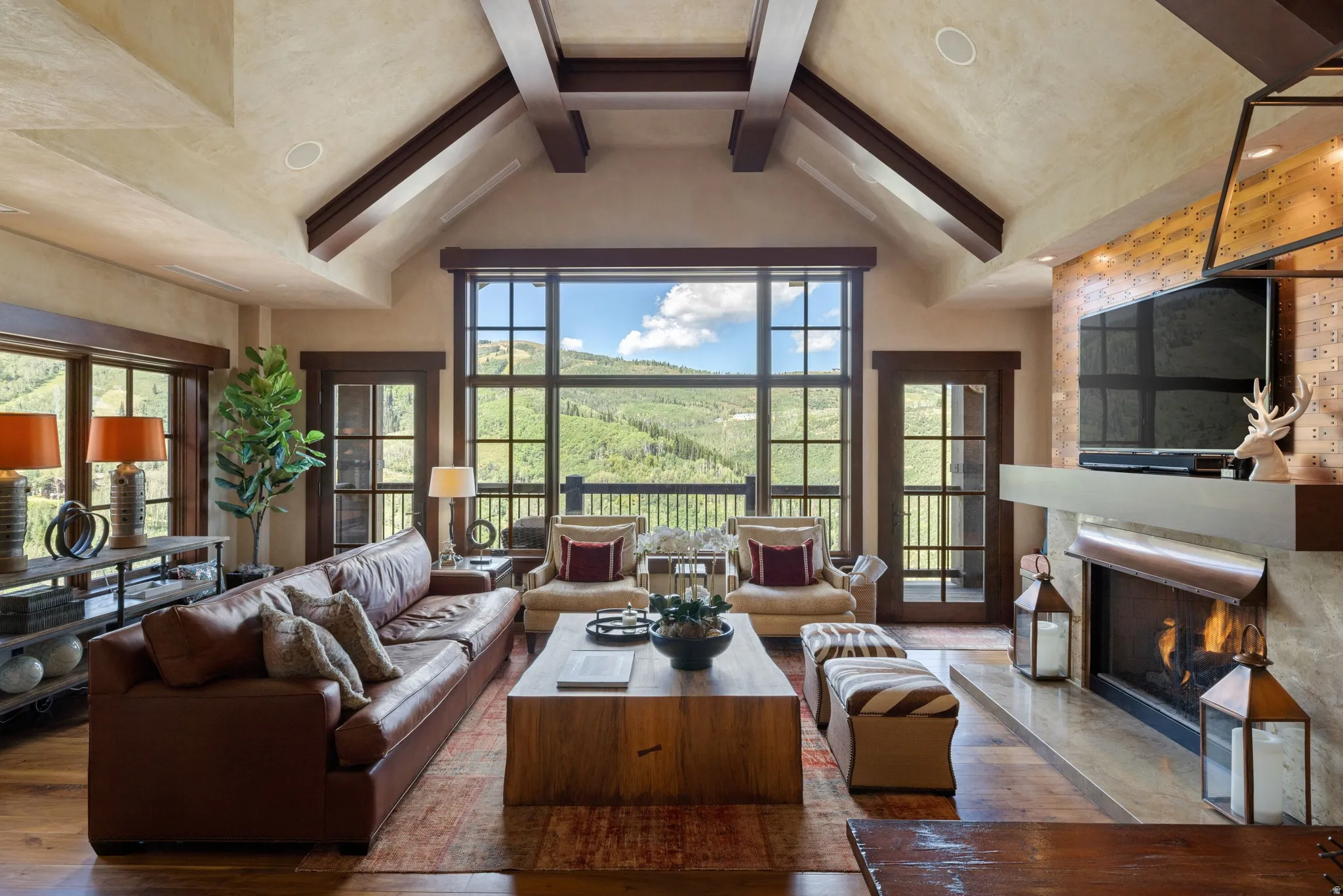 Vaulted ceiling with exposed wood beams, expansive window wall with grid detailing, wood-finish flooring, built-in fireplace with hearth, and a built-in media console