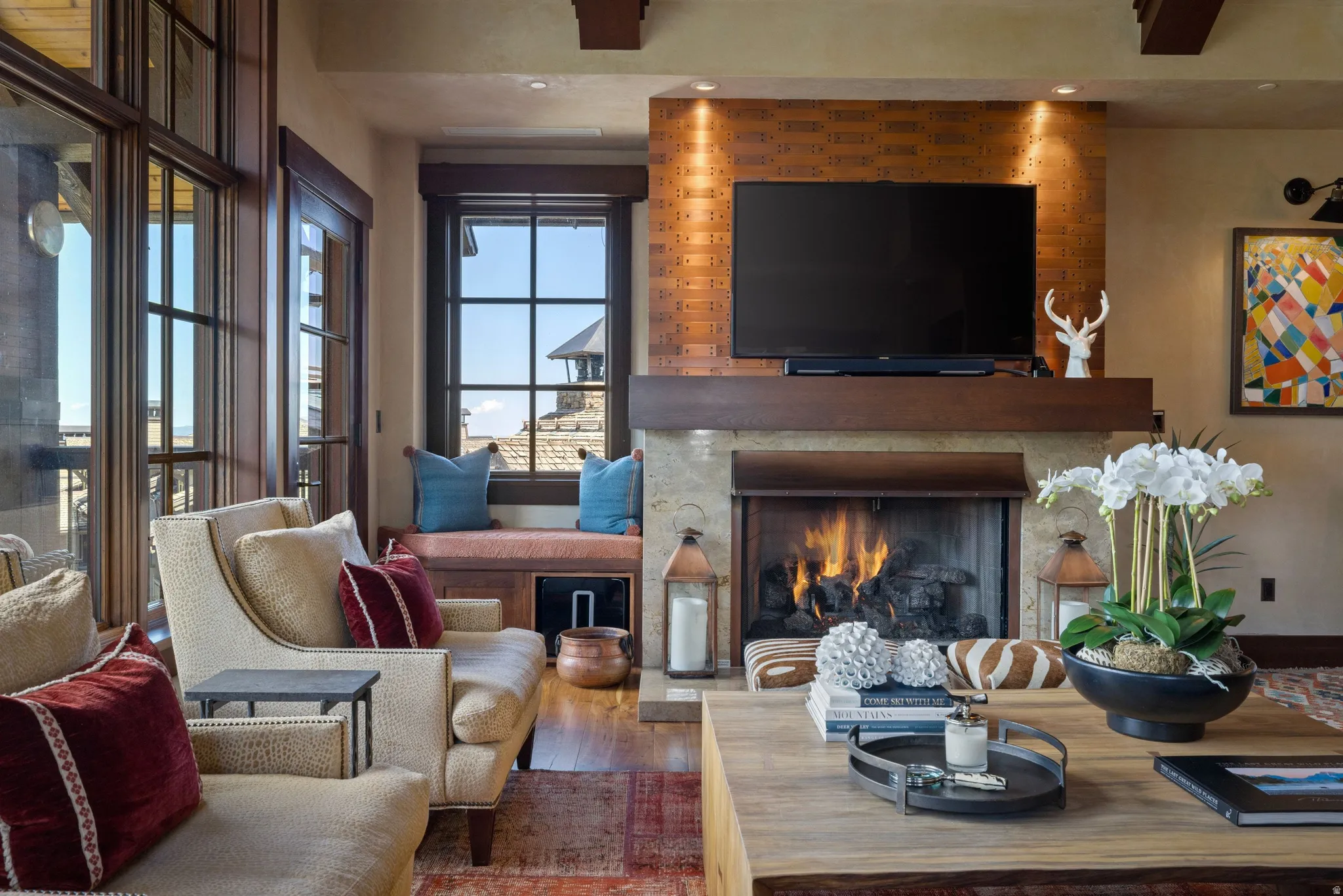 Fireplace with stone surround and wood mantel, large windows with dark wood frames, recessed lighting, and wood-finish flooring