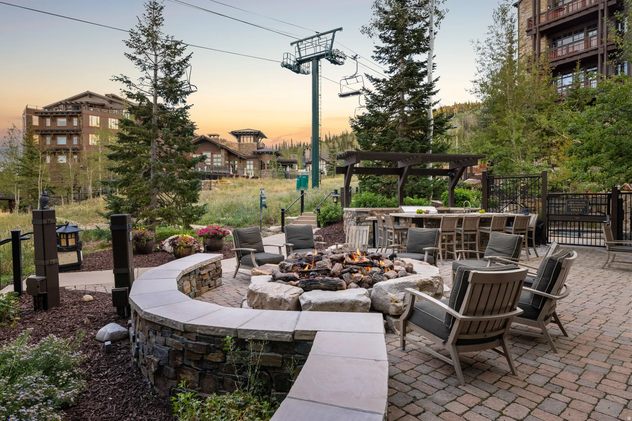 Brick paver patio featuring a stone-clad fire pit, built-in outdoor kitchen with bar seating, and a pergola