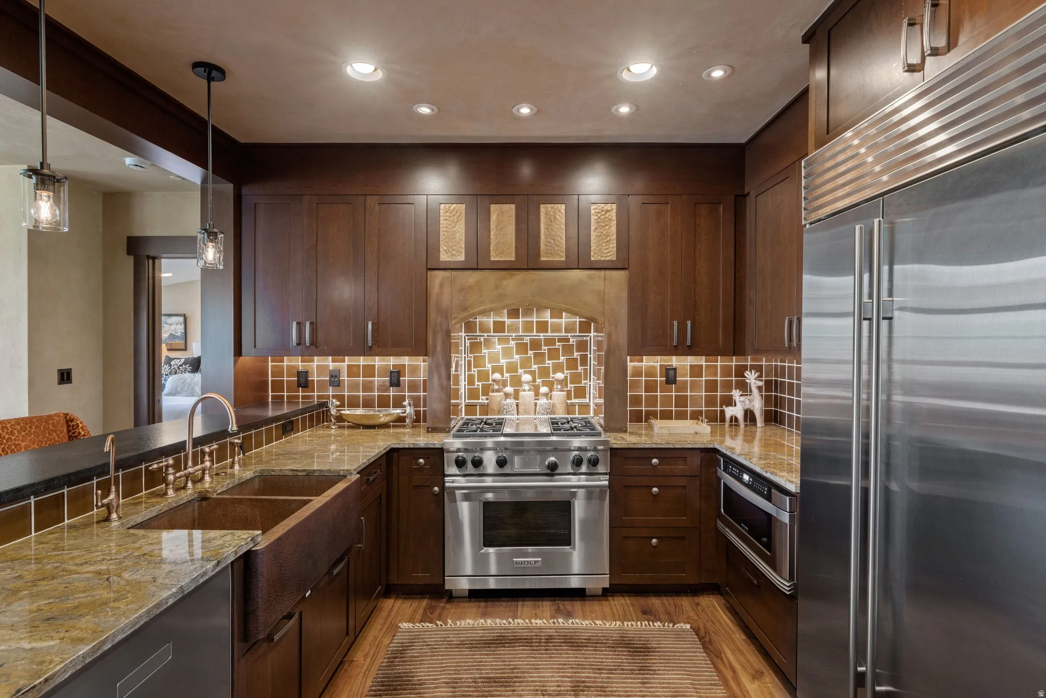 Chef's kitchen featuring custom dark wood cabinetry, stainless steel gas range and dual wall ovens, granite countertops, and a decorative tile backsplash in warm earth tones