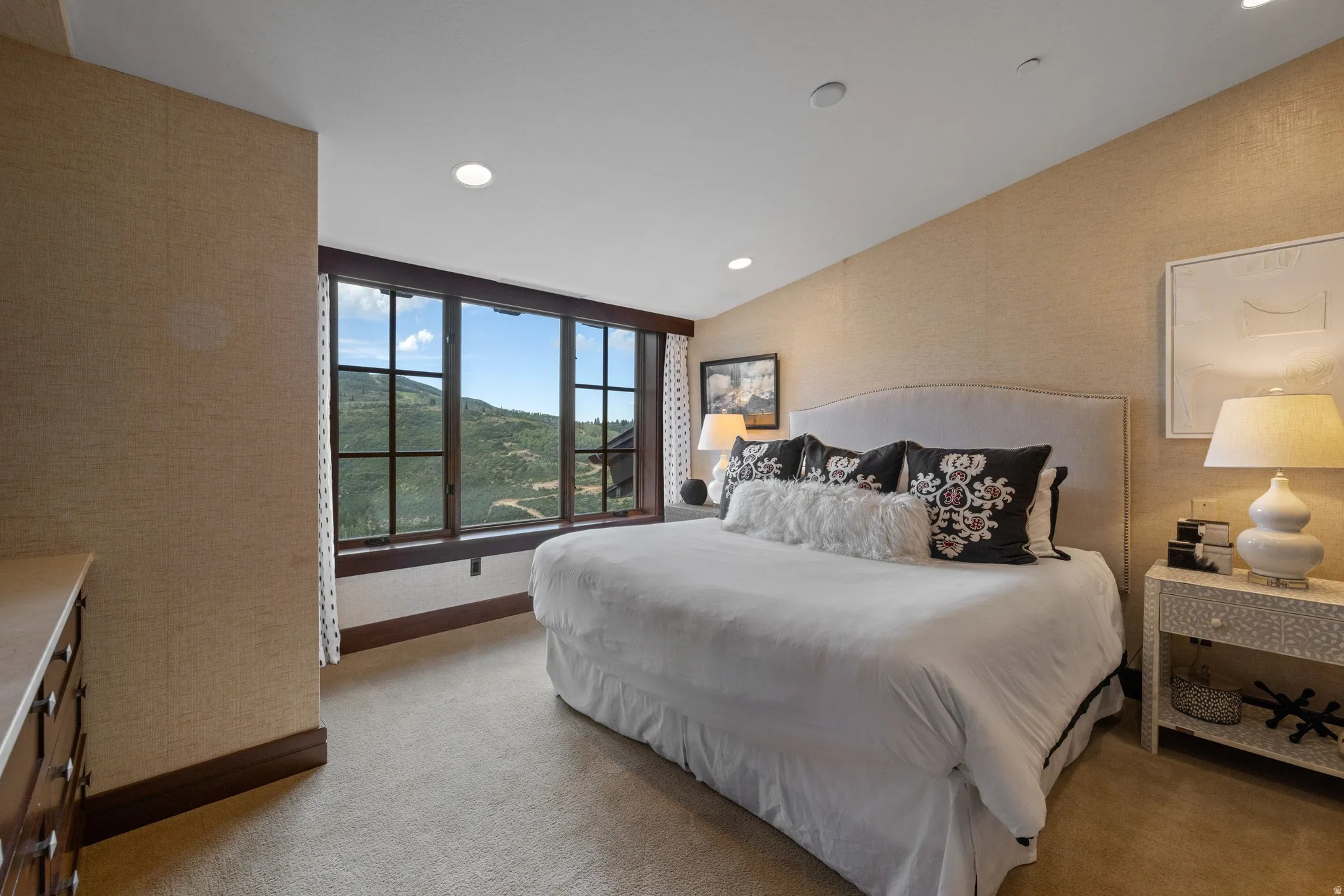 Expansive window with mountain scenery, recessed ceiling lighting, light-toned textured wall finish, and upholstered headboard