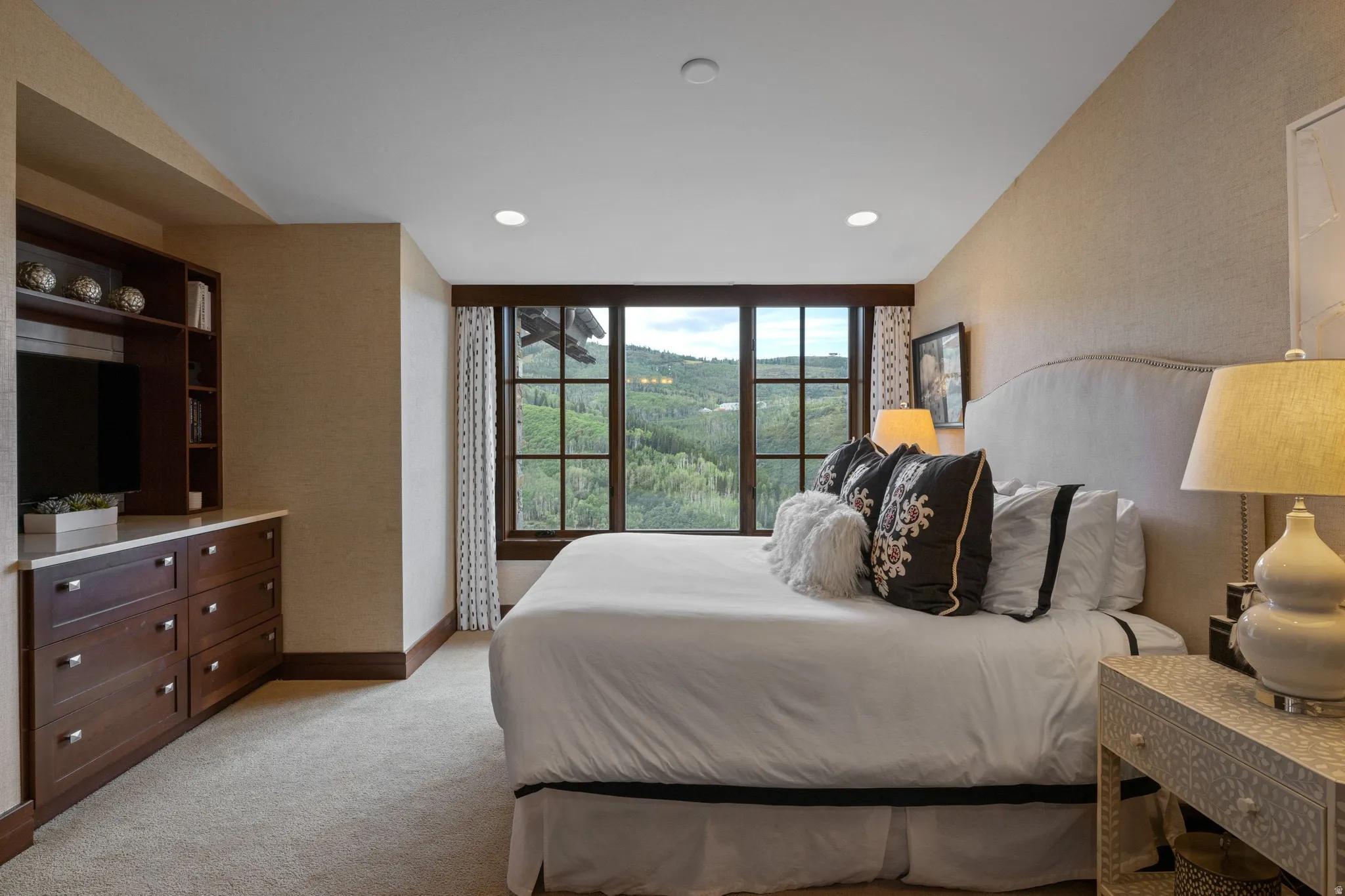 Built-in cabinetry with integrated shelving and drawers, large window with dark trim, textured wall covering, recessed ceiling lighting, and light-toned carpeting