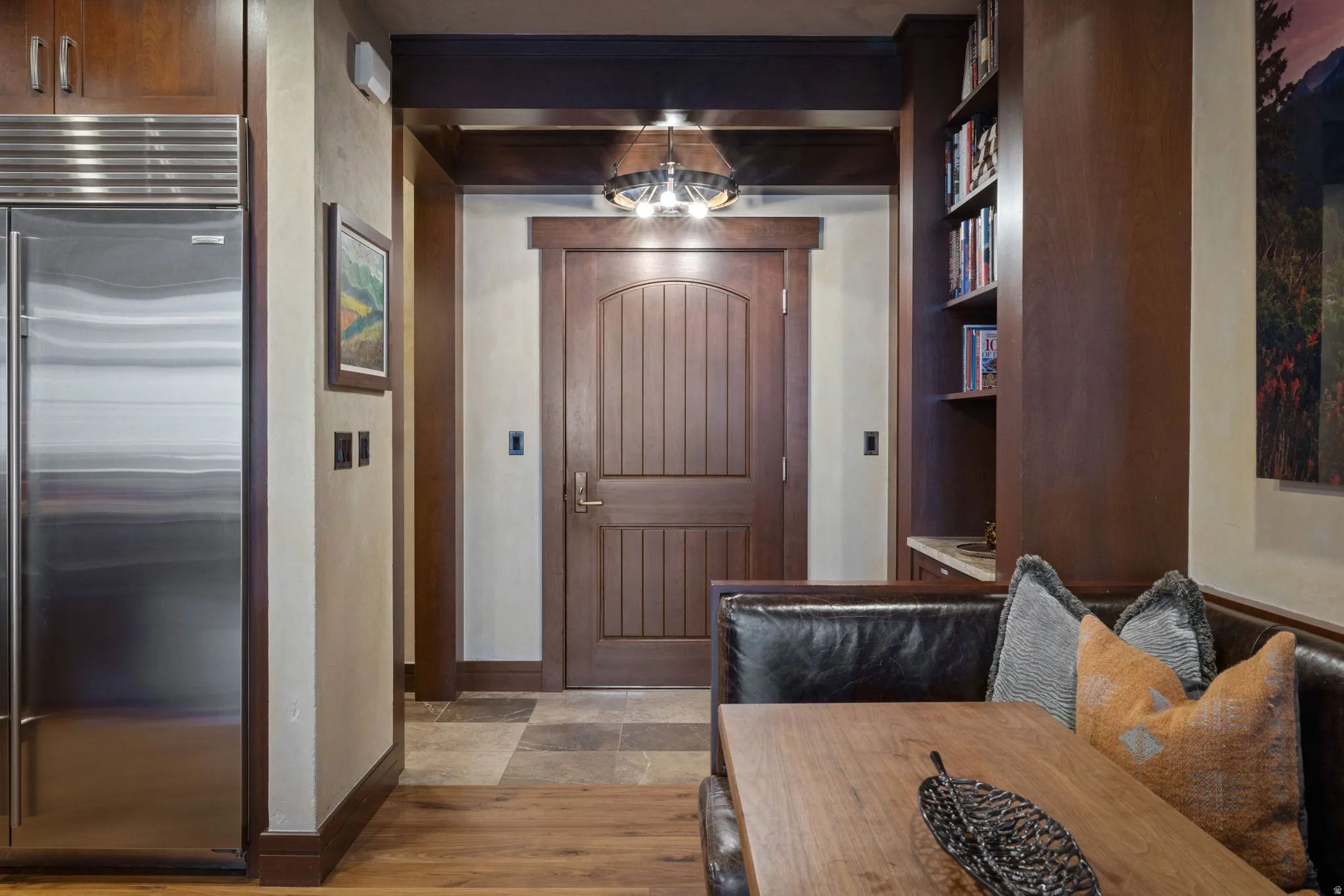 Built-in refrigeration with custom paneling, custom millwork door, built-in shelving, wood-finish flooring, and natural stone tile flooring