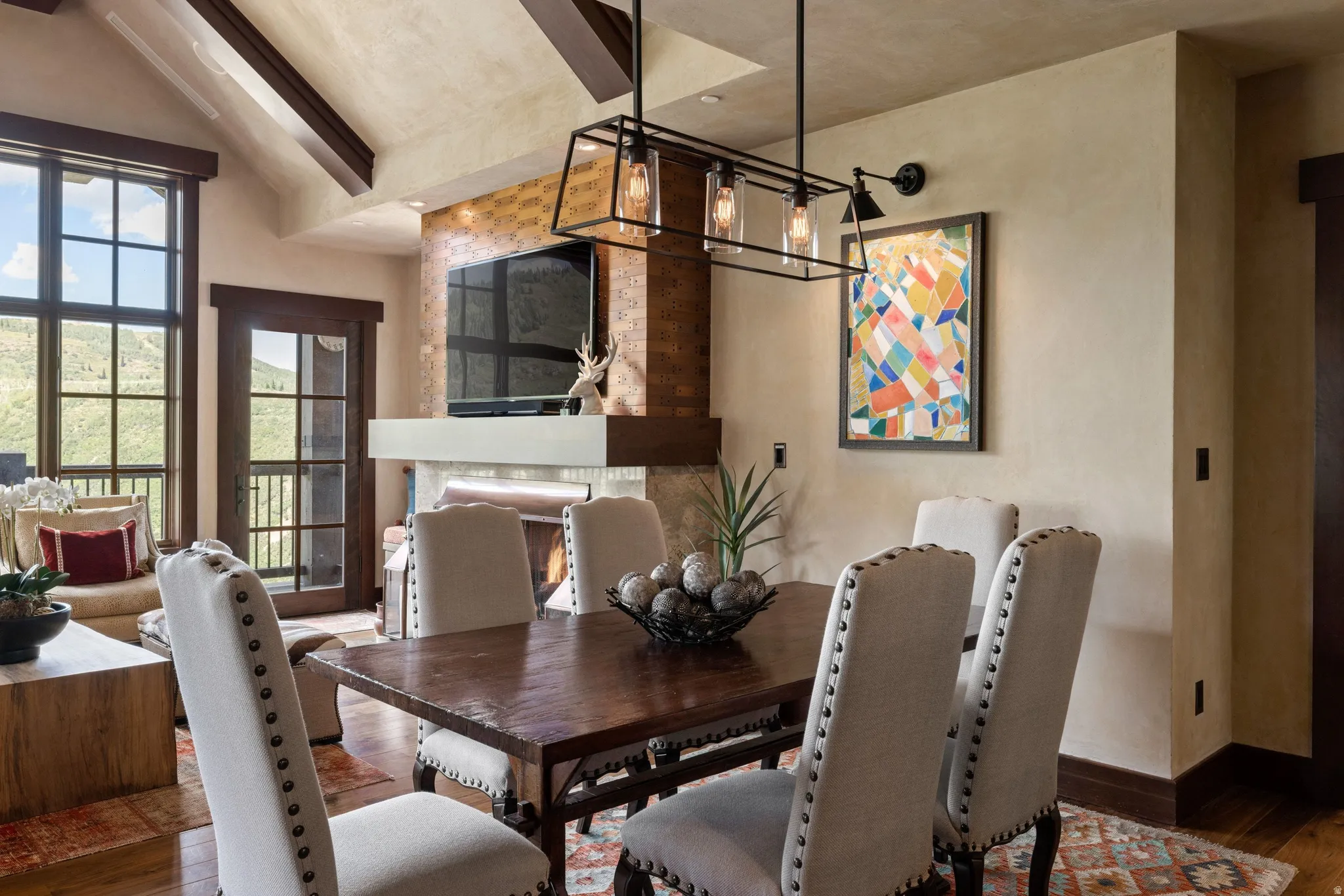 Vaulted ceilings with exposed beams, large windows, French doors, and a stone-clad fireplace