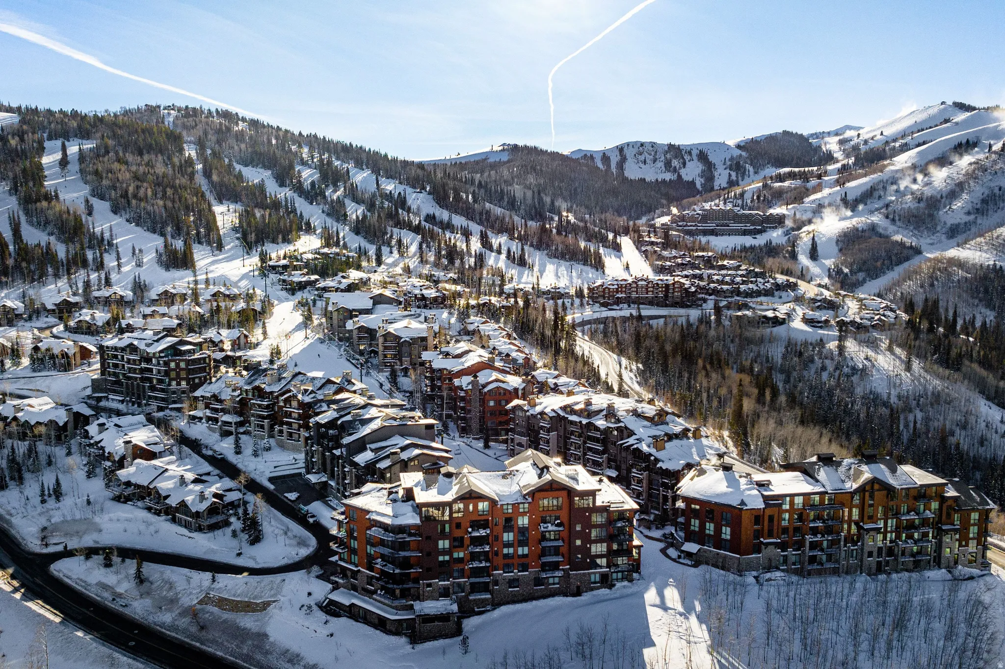 Snow-covered mountain community with varied architectural styles, surrounded by dense evergreen forests and visible ski slopes