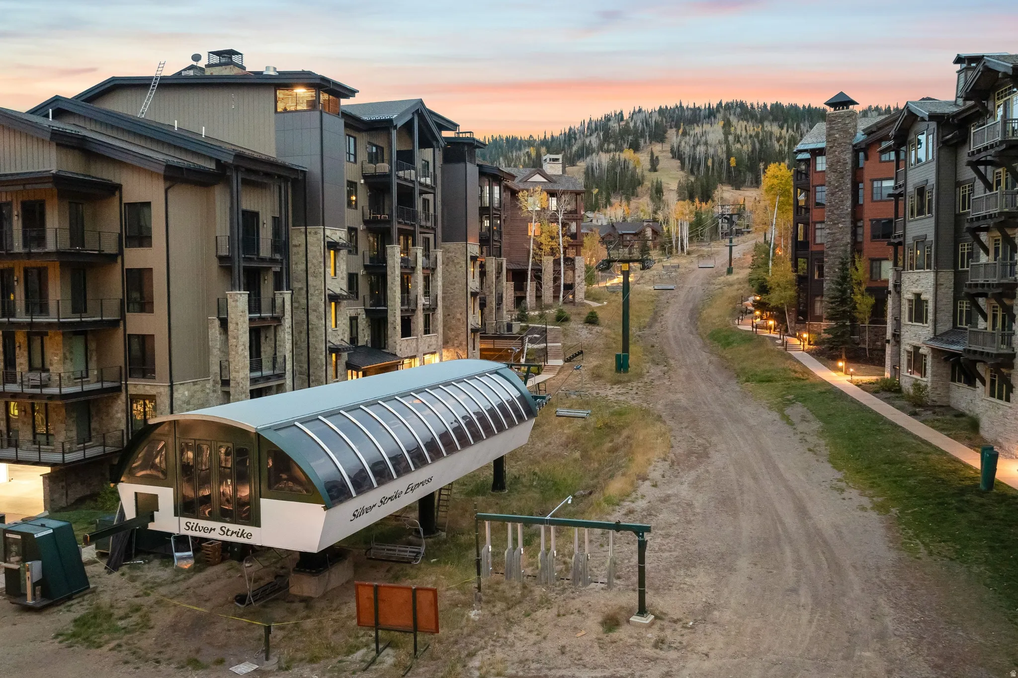 Contemporary mountain architecture with stone and wood siding, featuring private balconies, integrated lighting along pathways, and a prominent ski lift