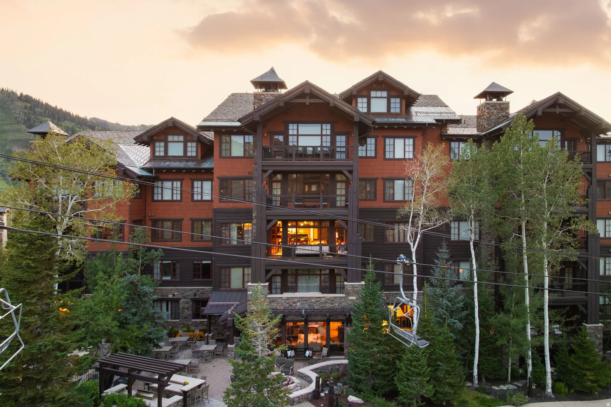 Multi-story property featuring extensive balconies, a stone and wood exterior, multiple rooflines, and a ground-level outdoor patio area