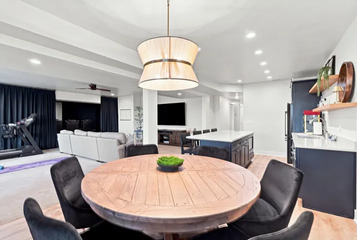 Spacious lower level featuring recessed lighting, a built-in kitchen island with seating, dark wood-finish cabinetry, and a light wood-finish round dining table