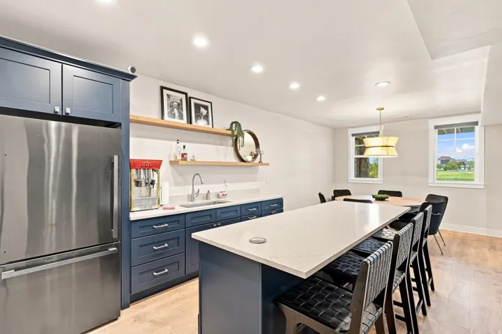Spacious kitchen with a large central island, stainless steel refrigerator, dark blue cabinetry, and light wood-finish flooring