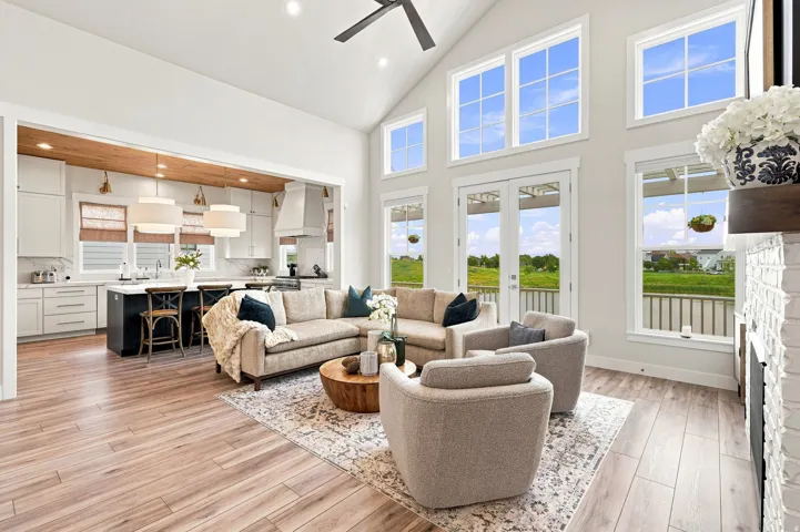 Vaulted ceiling, wood-finish flooring, white brick fireplace, white shaker cabinetry, and an island with counter seating
