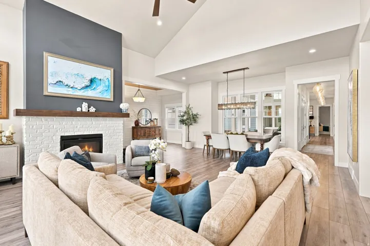 Vaulted ceilings, wood-finish flooring, a white brick fireplace with a wood mantel, and large windows with transom details