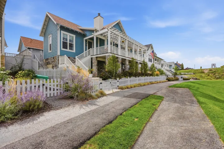 Blue siding exterior with white trim, multiple balconies, a white picket fence, and a landscaped front yard with green grass