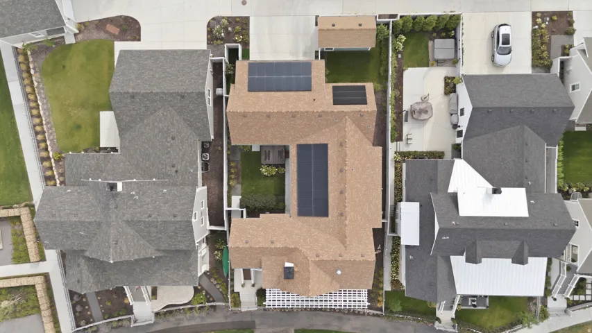 Gable roofline with solar panels, light brown shingles, concrete driveway, and a fenced backyard with a patio
