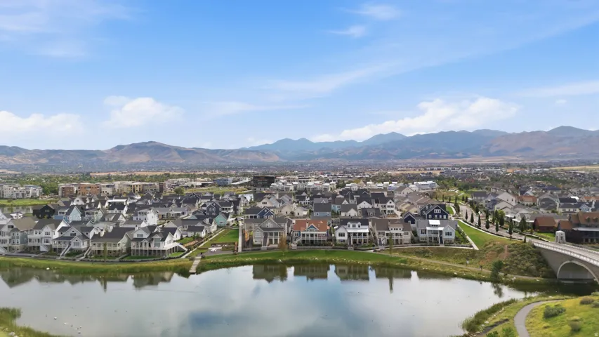Expansive residential community with waterfront properties, a dedicated walking path, and a stone arch bridge, all set against a mountainous backdrop