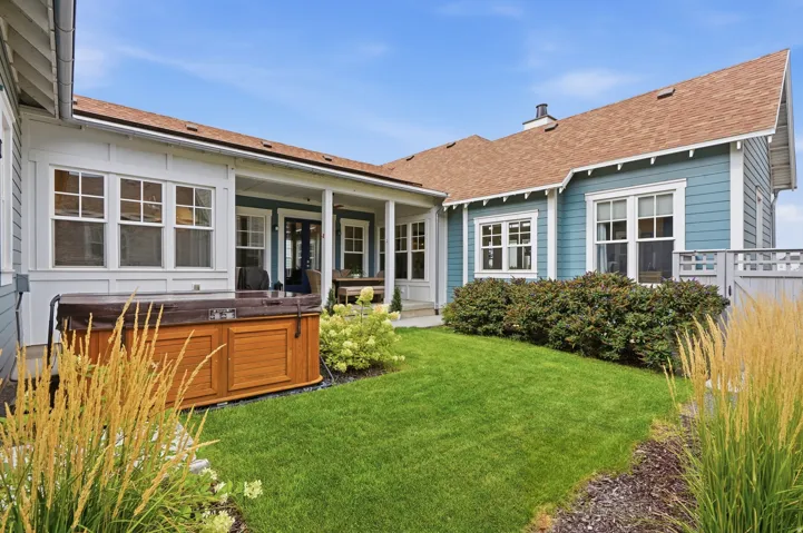 Manicured lawn with mature shrubs, a covered porch, and a built-in spa