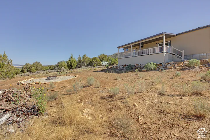 View of back of the house and yard. Full-length covered deck with white railing, exterior siding, and a stone-lined fire pit area
