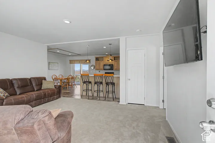 Recessed lighting, light-toned carpeting, a partial kitchen island with bar seating, and a dining area with wood-finish flooring