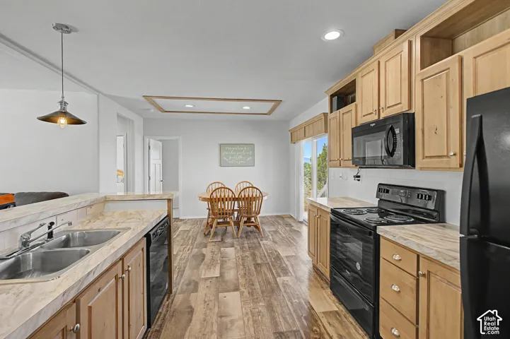 Kitchen featuring laminate flooring, light wood cabinetry, black appliances, and a double basin sink