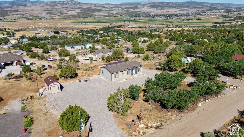 Ariel view of Expansive gravel driveway leading to a single-story residence with a brown shingle roof and a separate utility shed