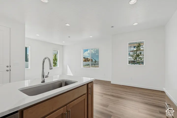 Kitchen island with a stainless steel undermount sink, gooseneck faucet, light-toned countertop, and wood-finish cabinetry