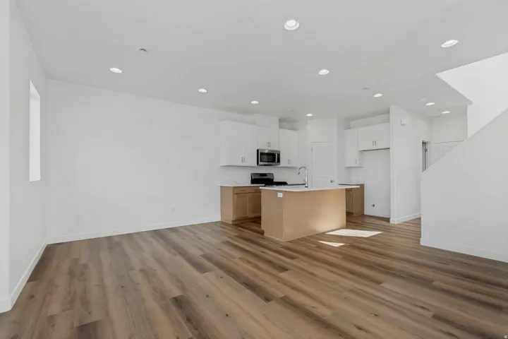 Open-concept living space with wood-finish flooring, recessed lighting, white cabinetry, and stainless steel appliances