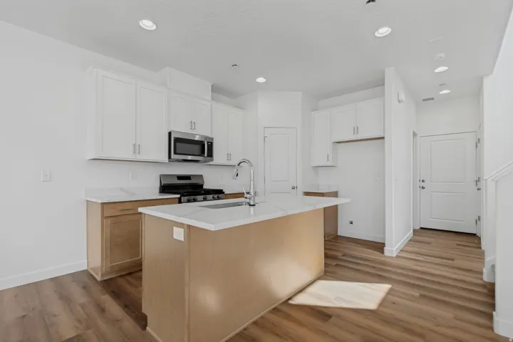 Kitchen featuring white upper cabinetry, light wood-finish lower cabinetry, a center island with a white countertop, stainless steel appliances, and wood-finish flooring
