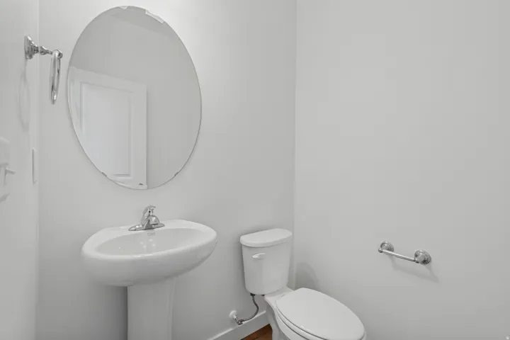 Pedestal sink with chrome faucet, oval frameless mirror, and white toilet